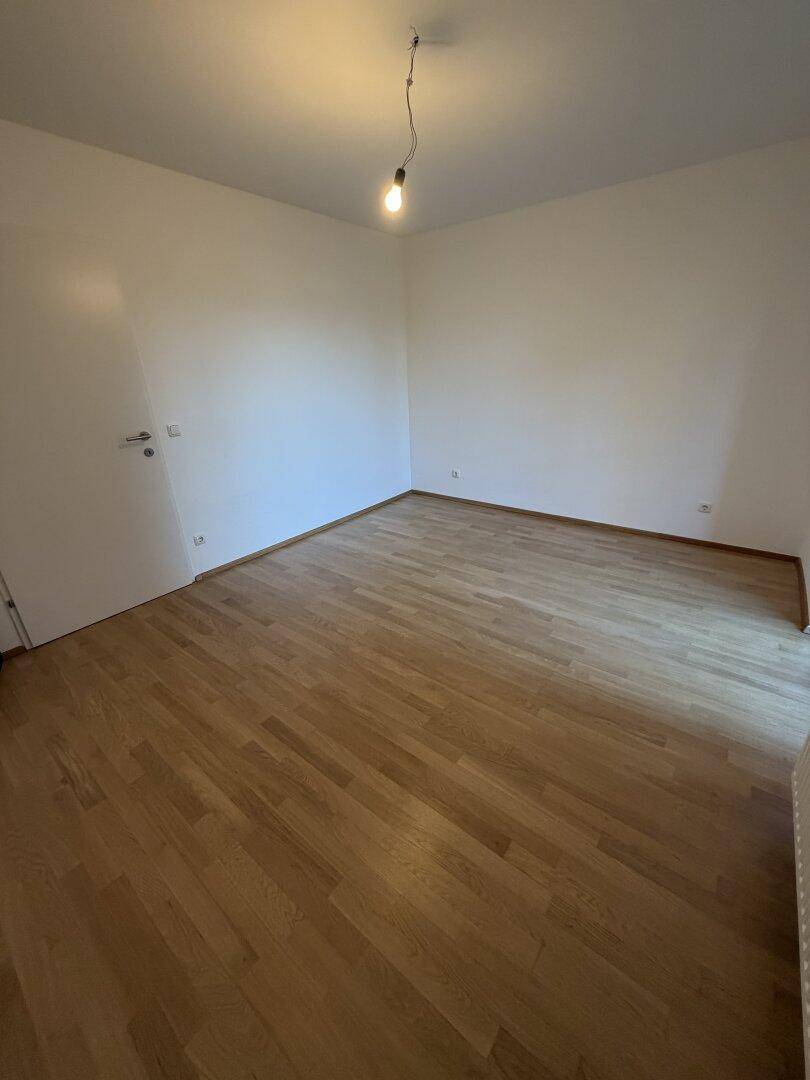 Leeres Zimmer mit hellem Holzfußboden und weißen Wänden, bereit zur individuellen Gestaltung.