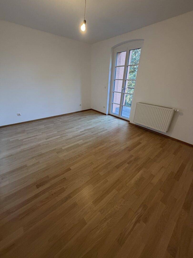 Helles Zimmer mit Holzfußboden und Zugang zu einem Balkon, der viel Licht spendet.