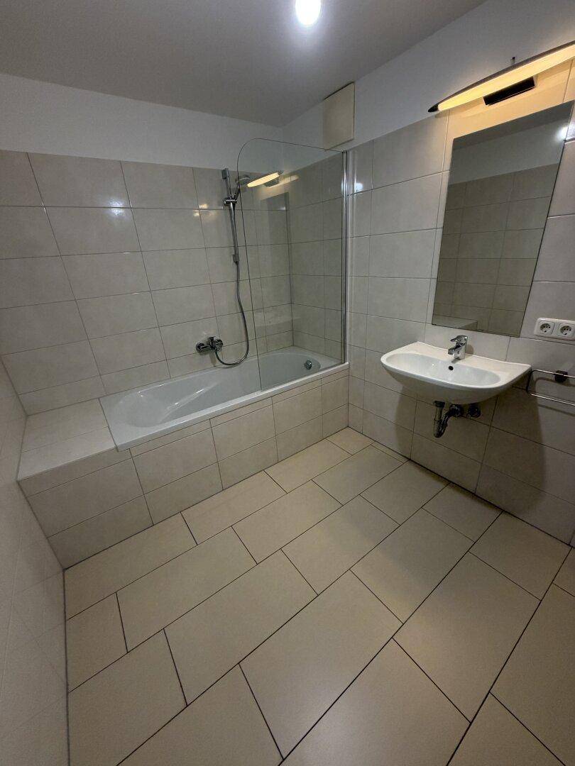 Modernes Badezimmer mit Badewanne, Dusche und Waschbecken, hell gefliest.