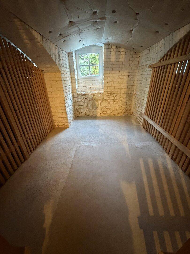 Kellerabteil mit kleinem Fenster, Ziegelwänden und Holzabtrennungen, ideal als Lagerraum.