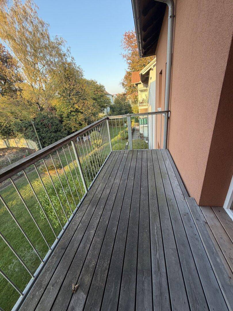 Leerer Holzbalkon mit Metallgeländer und Blick auf eine grüne Umgebung.