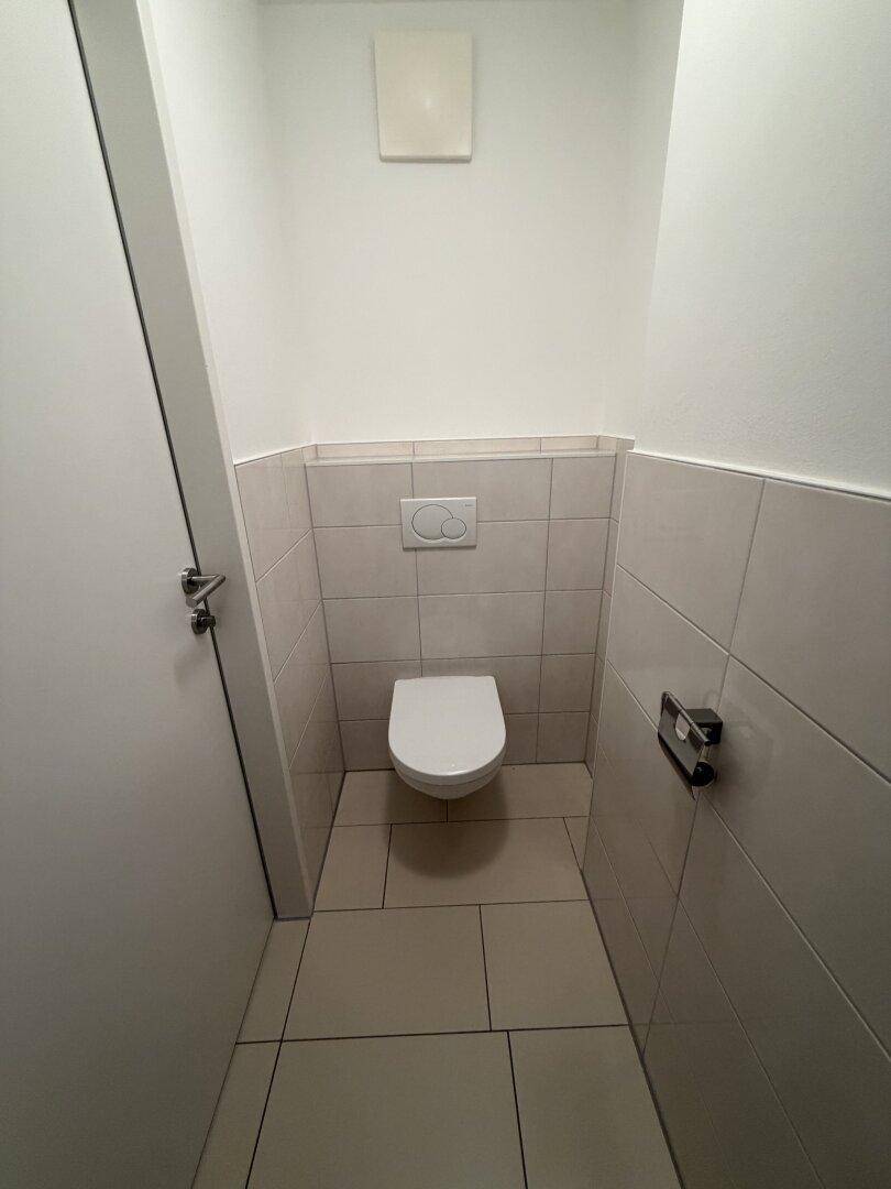 Separates WC mit wandhängender Toilette und hellen Fliesen an Boden und Wänden.