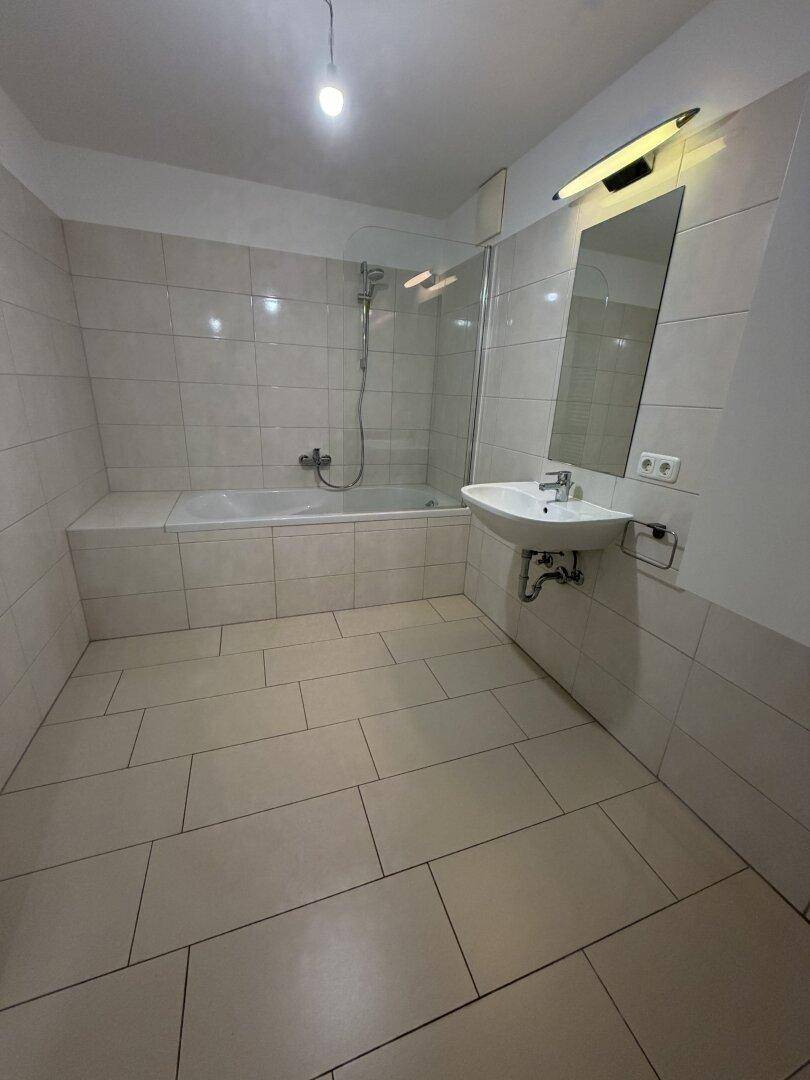 Badezimmer mit beigefarbenen Fliesen, Badewanne mit Duschwand und Einzelwaschbecken.