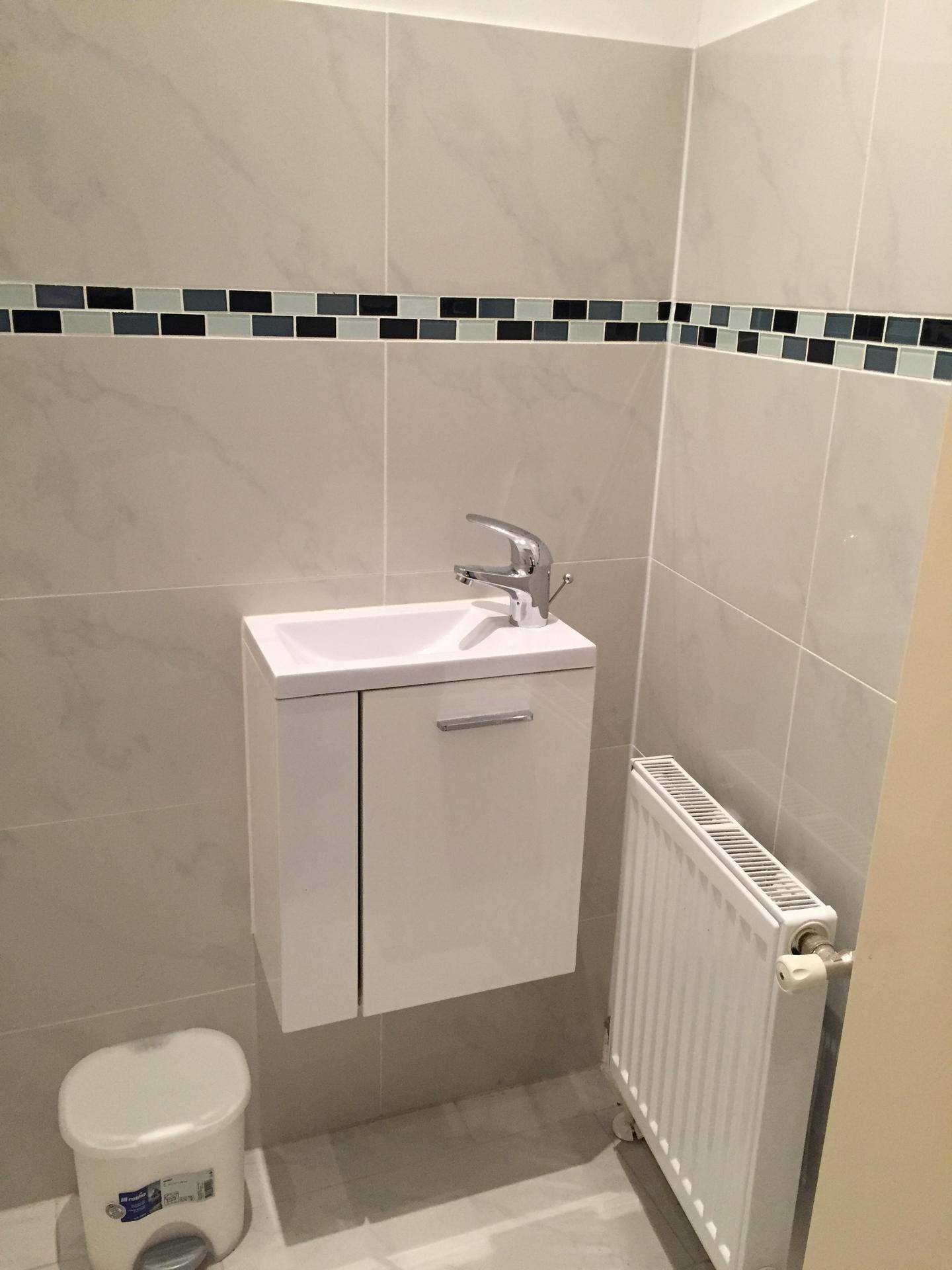 Kleines Gäste-WC mit modernem Hängewaschbecken, Heizkörper und hellen Fliesen an Wänden und Boden.