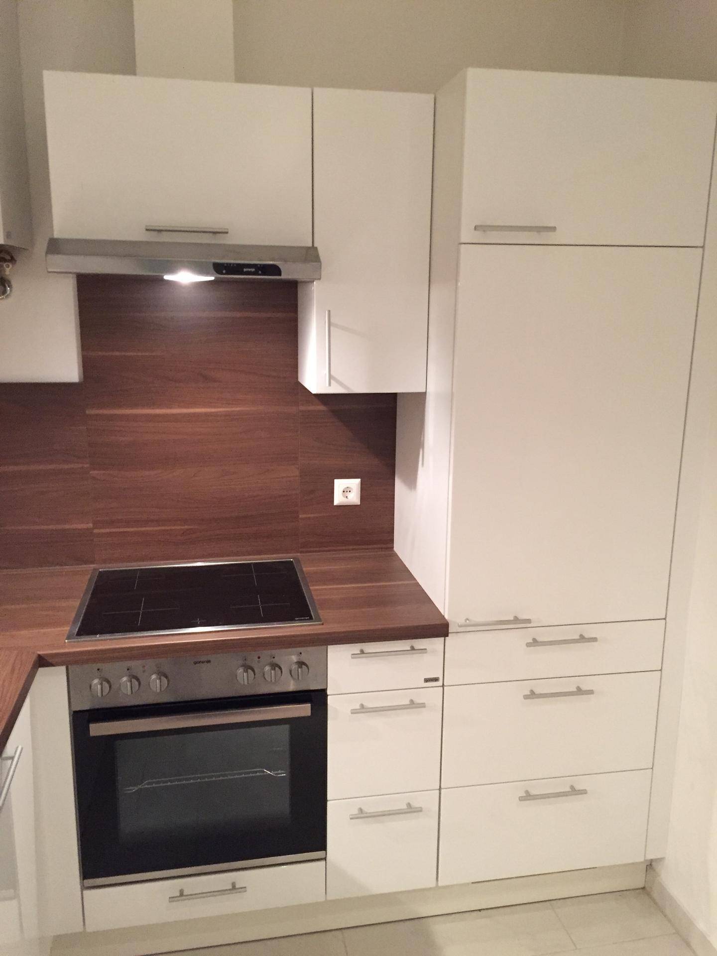 Kompakte, moderne Küche mit weißen Schränken, Holzoptik-Arbeitsplatte und integriertem Kochfeld und Backofen.