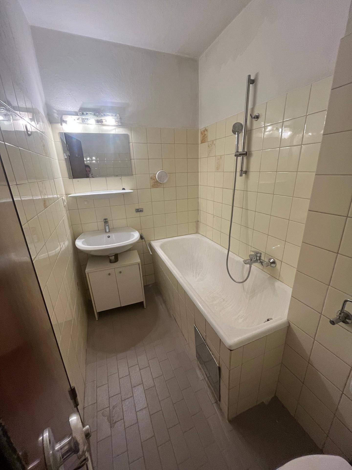 Badezimmer im Stil der 80er Jahre mit Badewanne, Waschbecken und gelben Fliesen, sanierungsbedürftig.