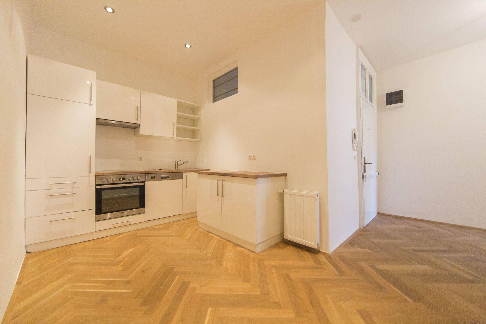 Moderne Küchenzeile mit weißen Schränken und integriertem Backofen in offenem Wohnbereich.
