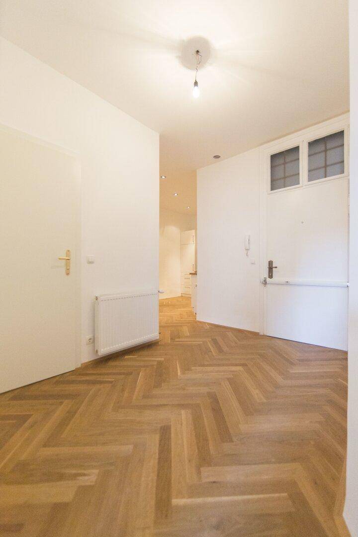 Heller Eingangsbereich mit Fischgrätparkett und Zugang zu weiteren Räumen.