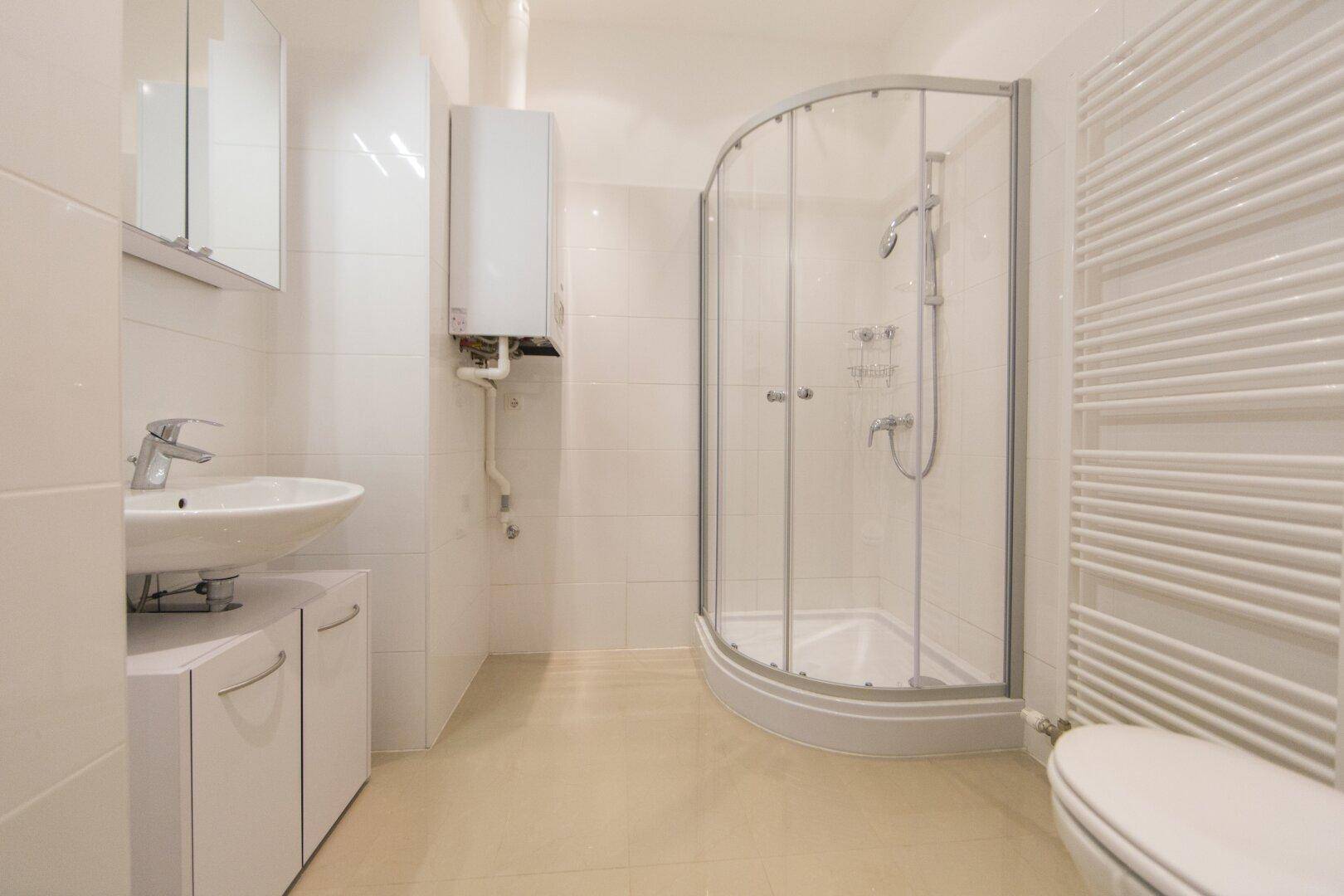 Helles Badezimmer mit Duschkabine, Waschbecken und beheiztem Handtuchhalter.