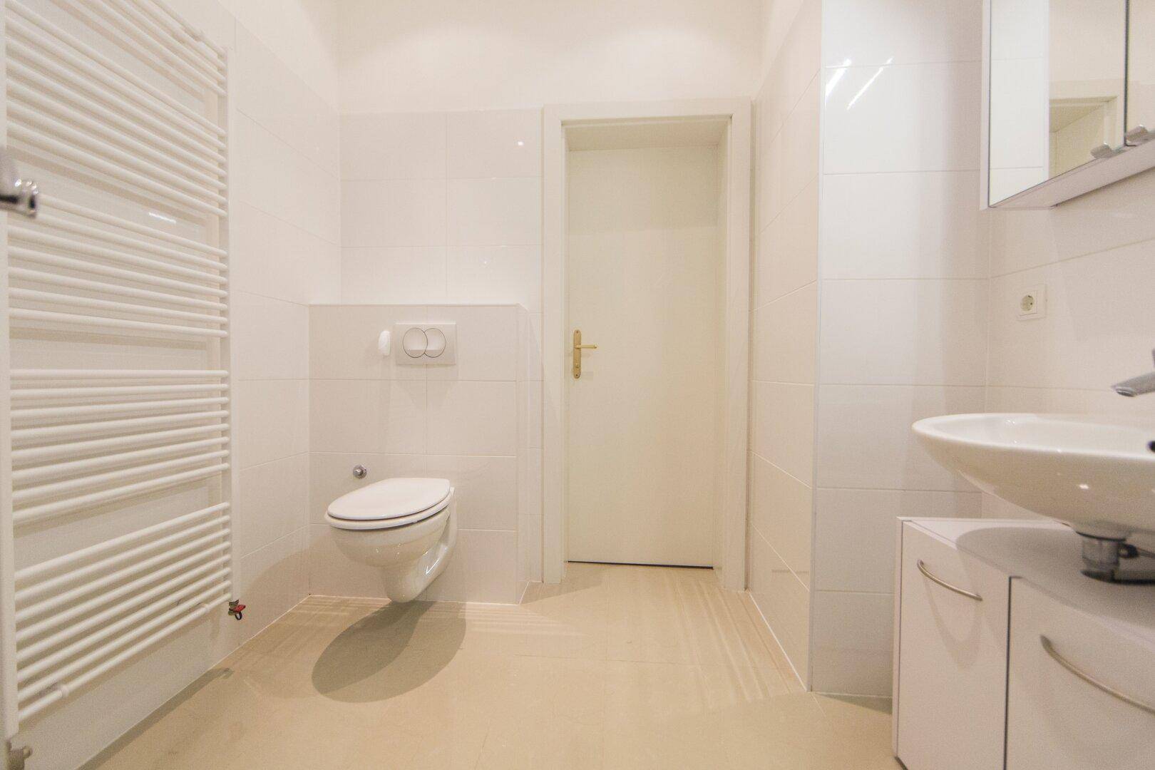 Funktionales Badezimmer mit wandhängendem WC, Waschbecken und beheiztem Handtuchhalter.