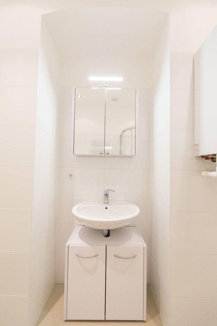 Waschbecken mit Unterschrank und Spiegelschrank im hell gefliesten Badezimmer.