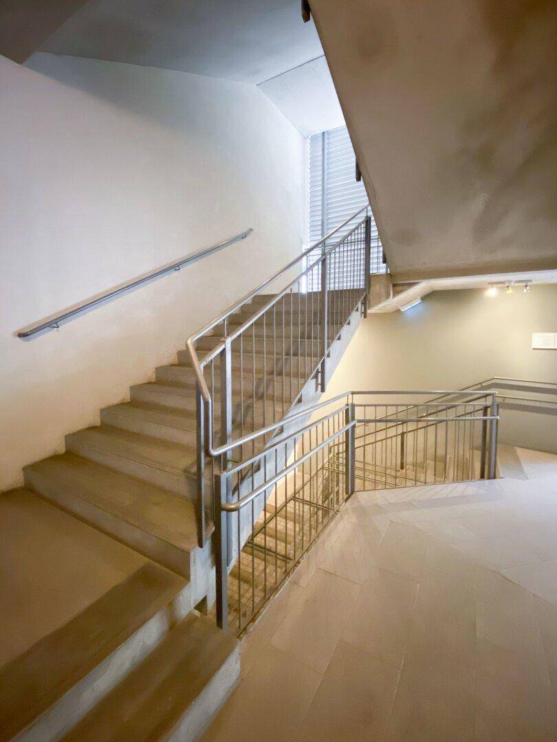 Geräumiges Treppenhaus mit Metallgeländer und hellen Stufen, das verschiedene Ebenen verbindet und gut gepflegt ist.