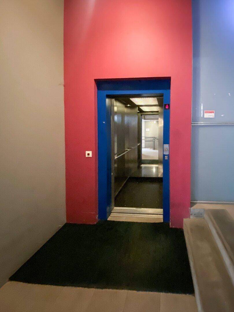 Moderner Aufzugsbereich mit leuchtend roten Wänden und einem offenen Aufzug, der Zugang zu den Etagen bietet.