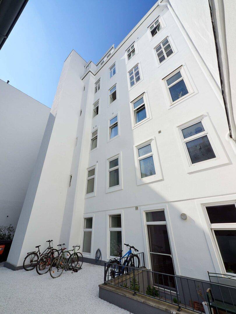 Weiße Gebäudefassade im Innenhof mit vielen Fenstern und Fahrrädern im Vordergrund.