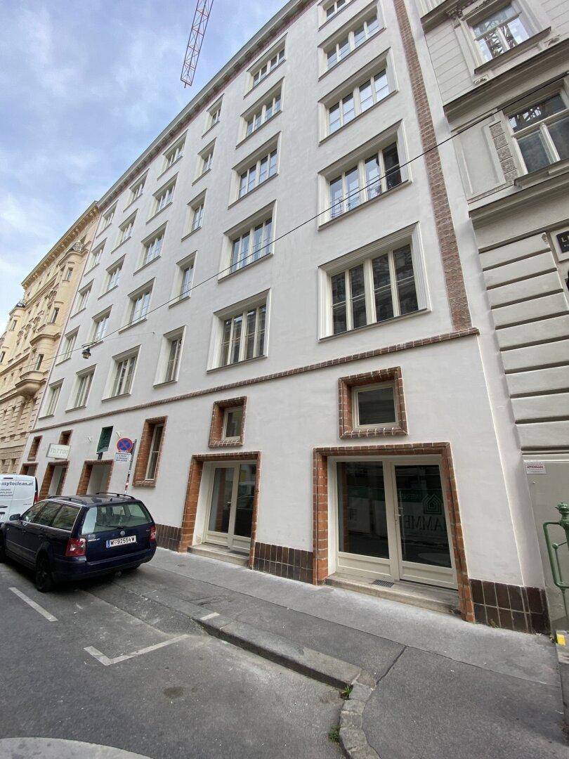 Mehrstöckiges Gebäude mit weißer Fassade, vielen Fenstern und Ziegelakzenten an der Straßenseite.