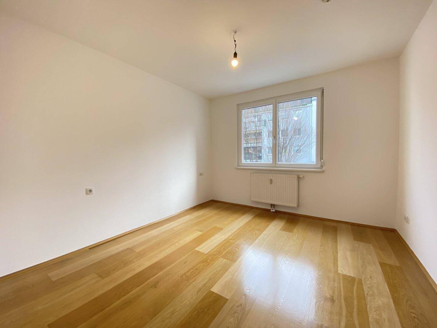 Helles Schlafzimmer mit Holzparkettboden und einem Fenster mit Blick nach draußen.