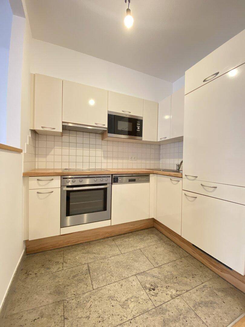 Kompakte Einbauküche mit hellen Schränken, Holztheke und modernen Geräten.