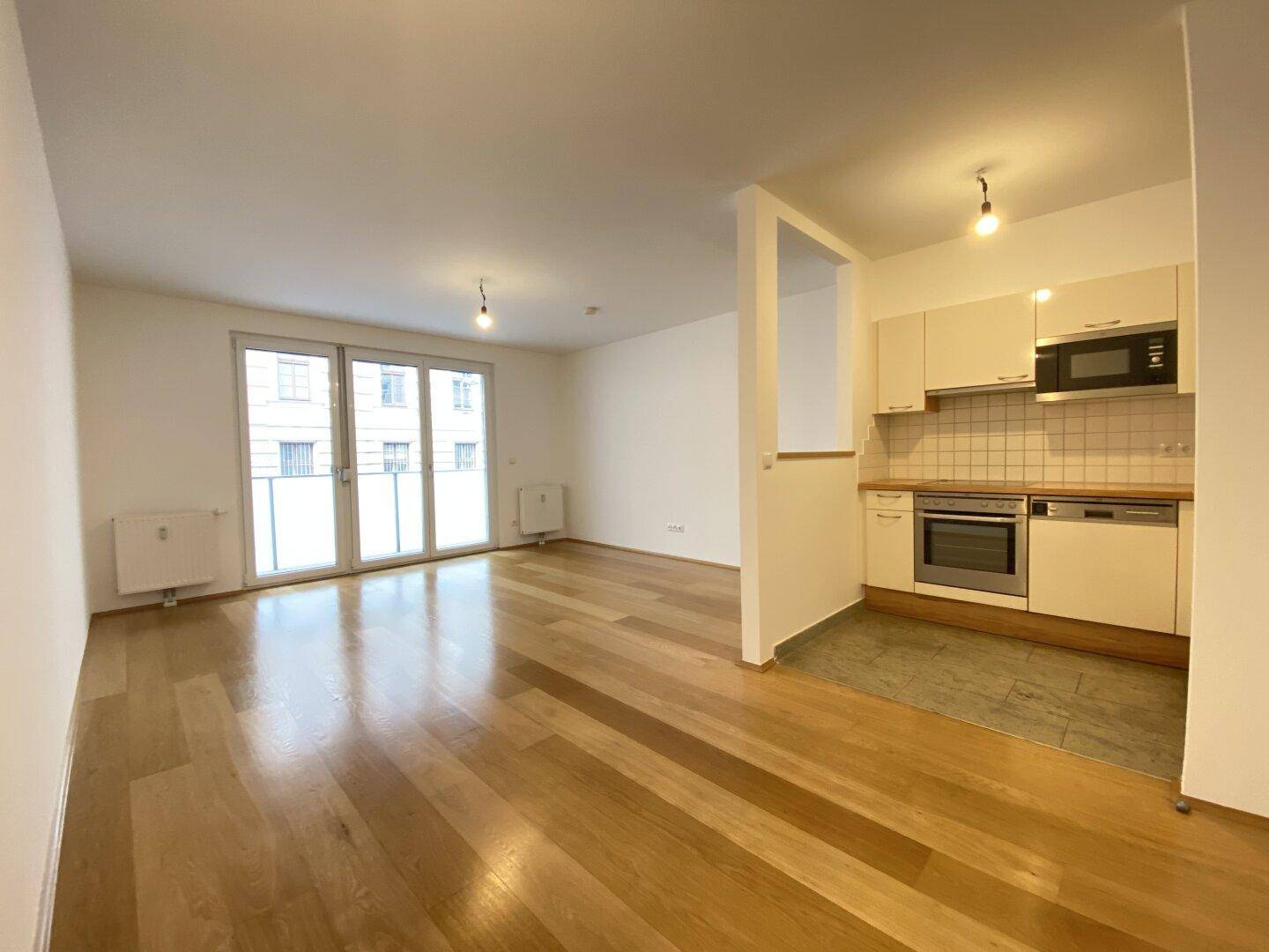 Offener Wohnbereich mit integrierter Küche und Zugang zu einem Balkon.