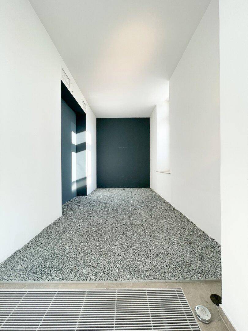 Moderner Flur mit weißen Wänden und einem dekorativen Kiesbett auf dem Boden, das einen einzigartigen Akzent setzt.