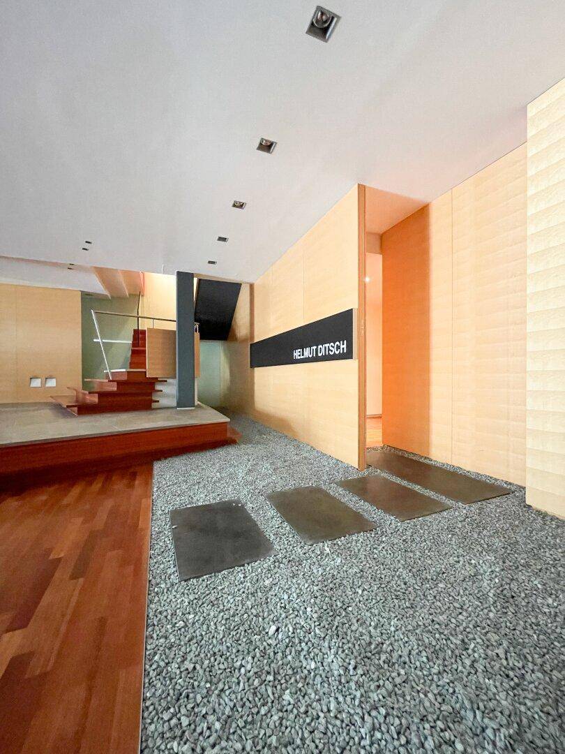 Moderner Eingangsbereich mit Kiesboden, Holzvertäfelung und einer eleganten Treppe, die nach oben führt.