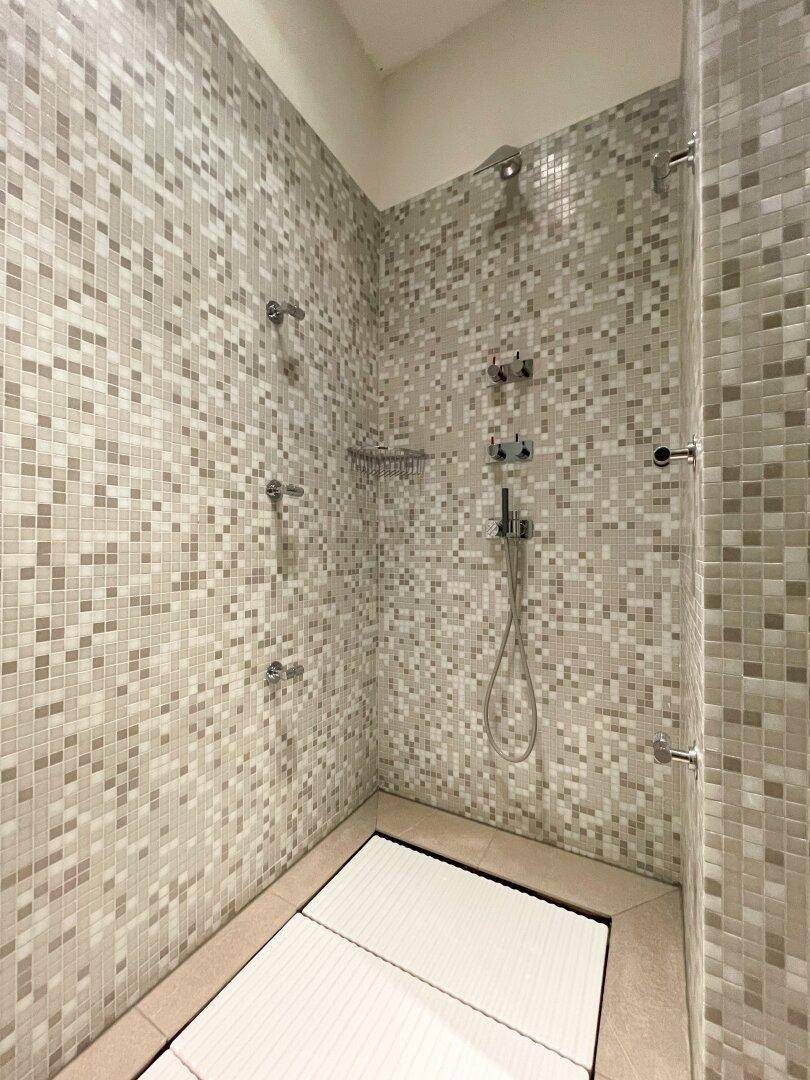 Geräumige Duschkabine mit Mosaikfliesen an den Wänden und mehreren Duschköpfen für ein luxuriöses Erlebnis.