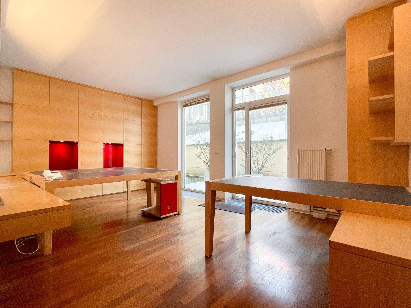 Geräumiges Büro mit großen Fenstern, Holzboden und integrierten Möbeln, bietet viel Tageslicht.