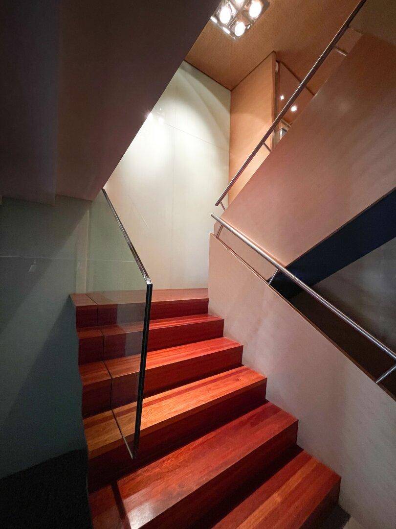 Moderne Holztreppe mit Glasgeländer und indirekter Beleuchtung, die zu den oberen Etagen führt.