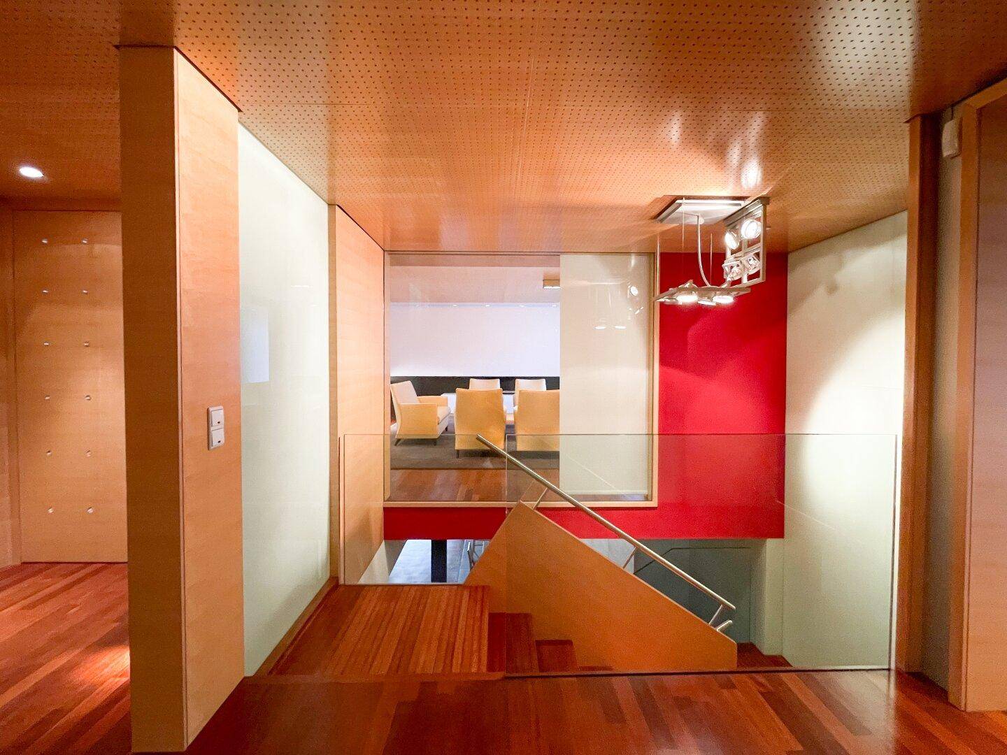 Heller Flur mit Holzvertäfelung und Blick auf eine moderne Treppe mit Glasgeländer.