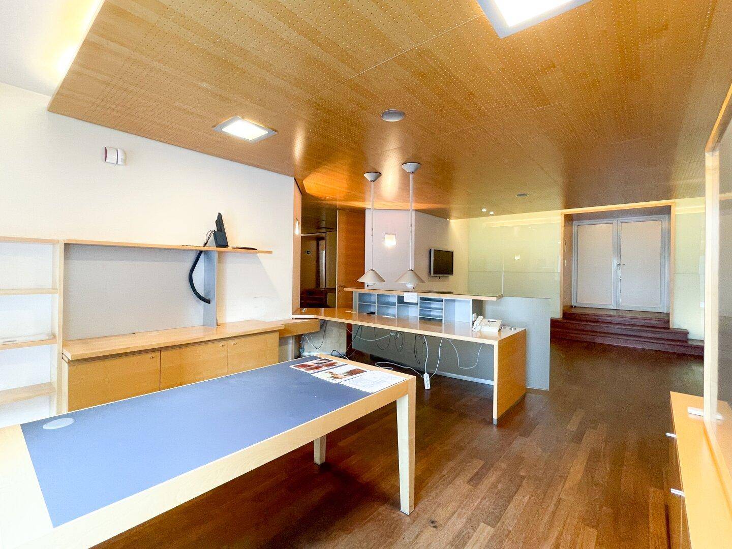 Empfangsbereich mit Holzboden, Theke und integrierten Arbeitsplätzen, ideal für Kundenempfang.