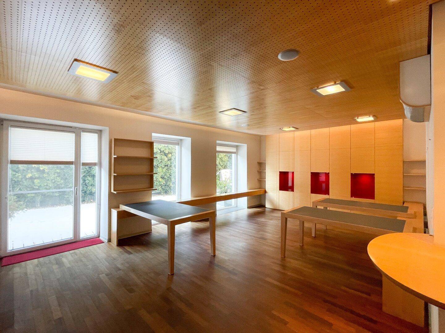 Heller Büroraum mit Holzboden, großen Fenstern und Zugang zu einem Balkon, bietet viel Tageslicht.