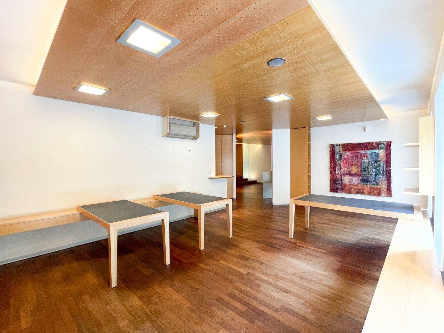 Geräumiger Büroraum mit Holzboden, integrierten Tischen und einem farbenfrohen Wandteppich als Akzent.