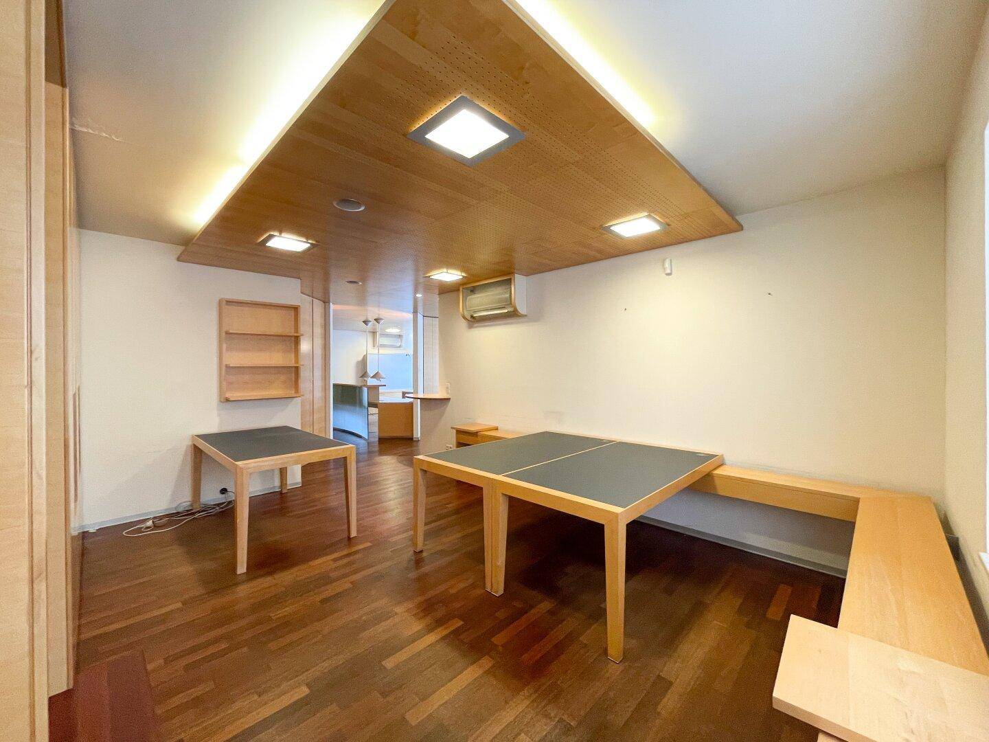 Moderner Büroraum mit Holzboden, integrierten Tischen und Klimaanlage, bietet eine komfortable Arbeitsumgebung.