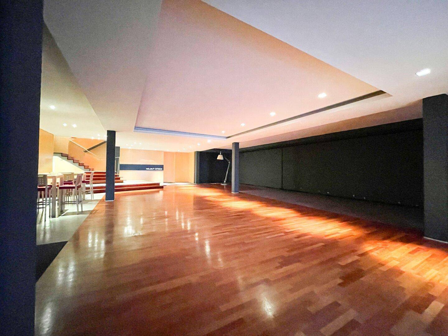 Geräumiger, offener Gewerberaum mit glänzendem Holzplankenboden, einer Bar und einer modernen Treppe im Hintergrund.