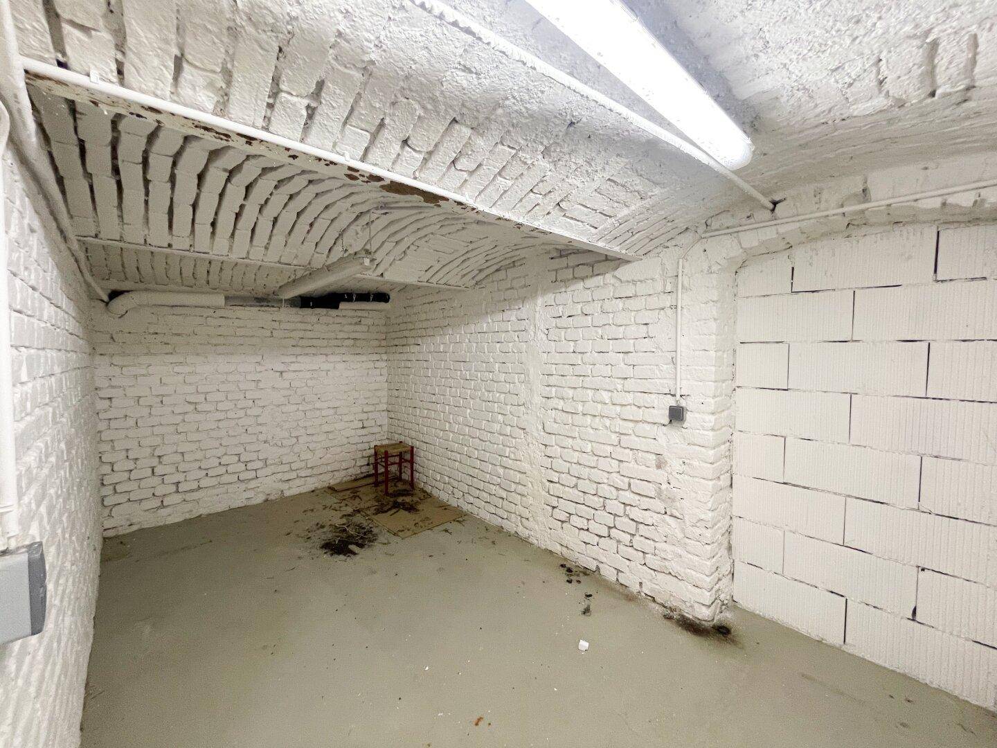Kellerraum mit weiß gestrichenen Ziegelwänden, Tonnengewölbe und einer Wand aus Porenbetonsteinen.