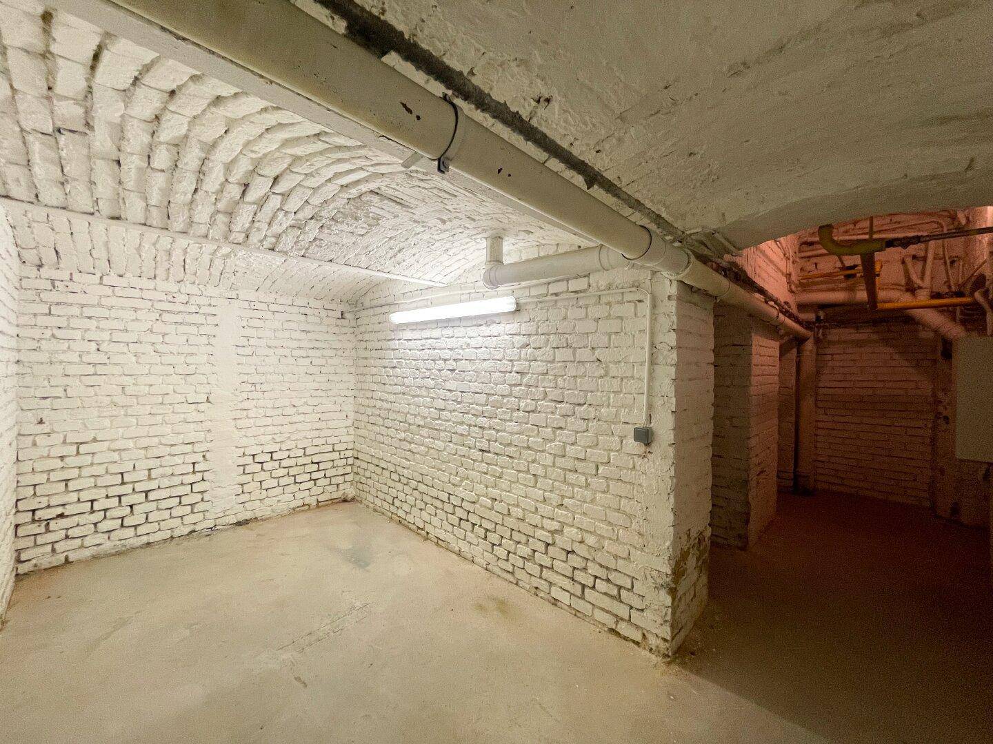 Kellerraum mit weiß gestrichenen Ziegelwänden, Tonnengewölbe und sichtbaren Leitungen an der Decke.