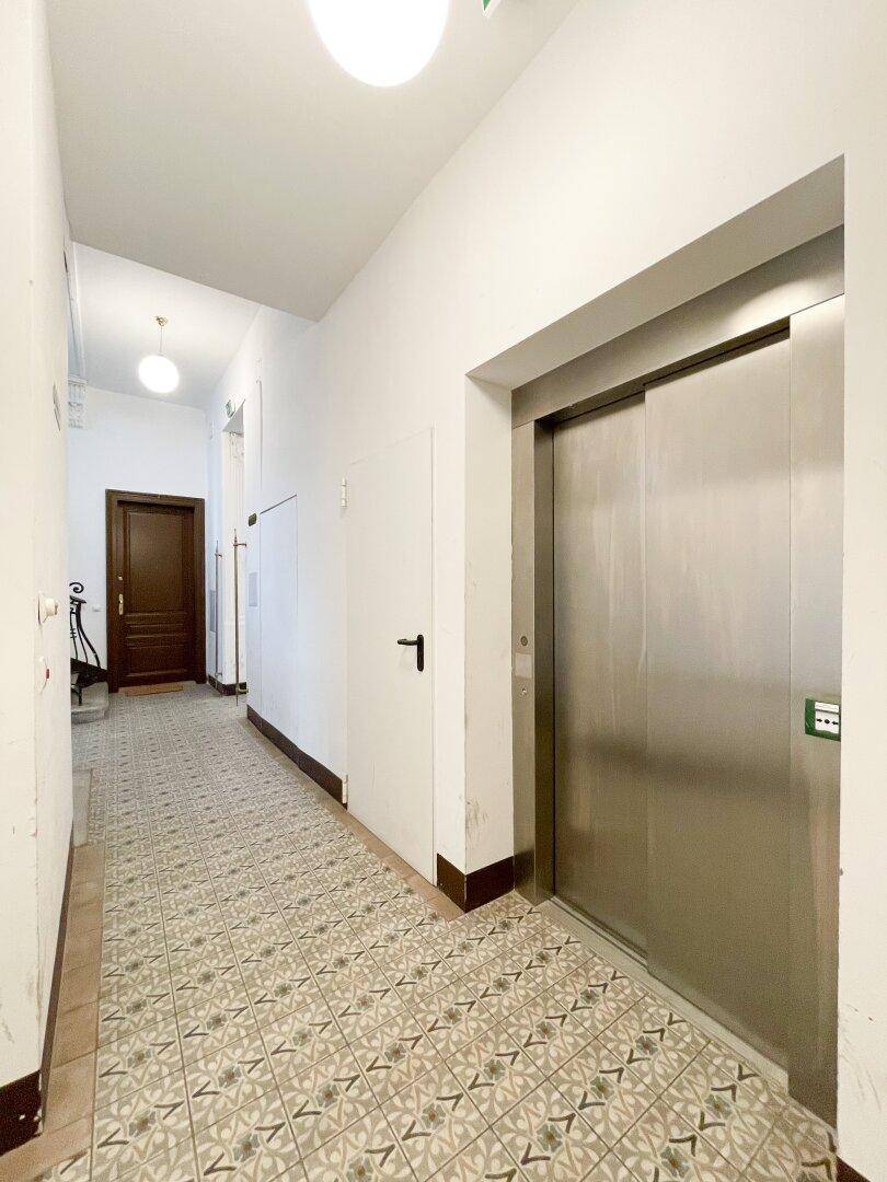 Heller Flur mit Aufzug und gemusterten Bodenfliesen, der zu weiteren Wohnungen führt.