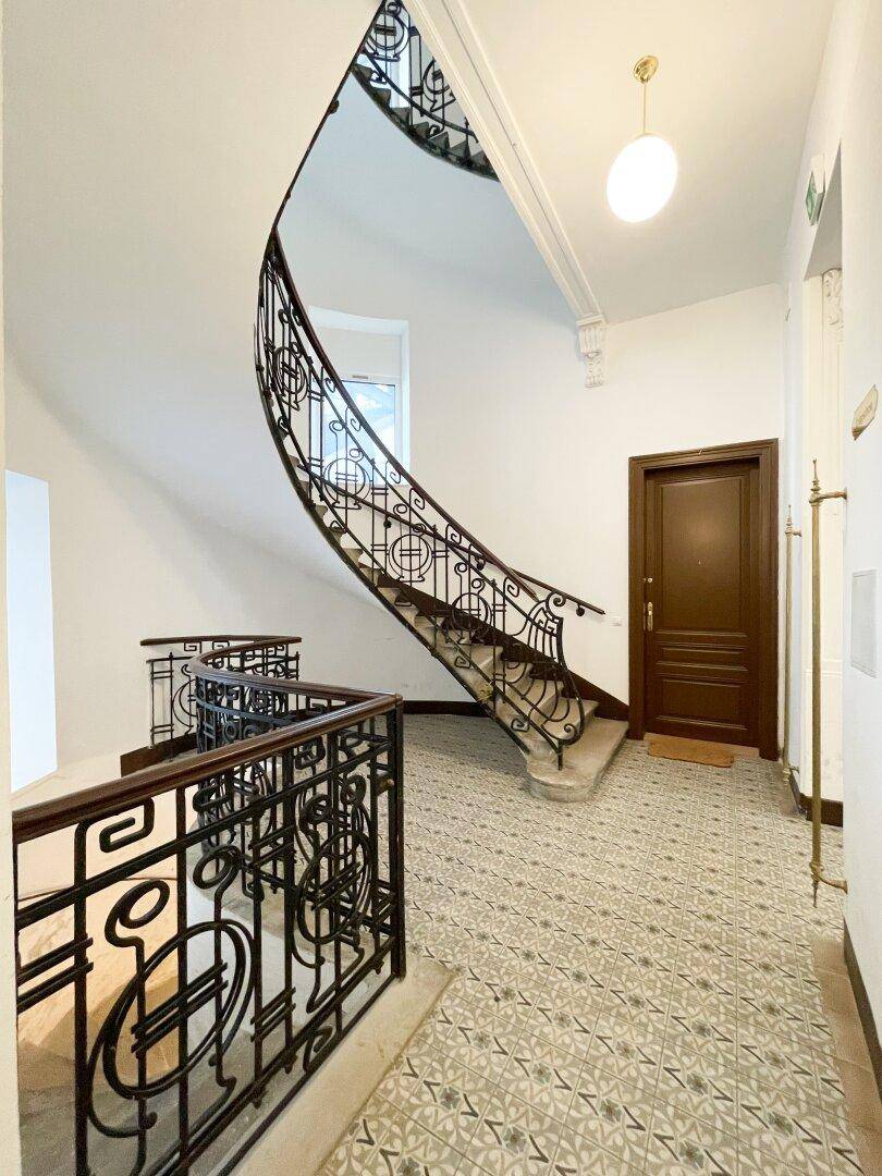Elegantes Treppenhaus mit geschwungenem Geländer aus Schmiedeeisen und gemusterten Bodenfliesen.