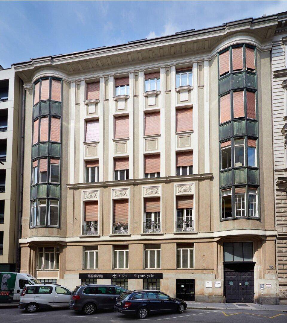 Historische Gebäudefassade mit vielen Fenstern, Fensterläden und geparkten Autos davor.