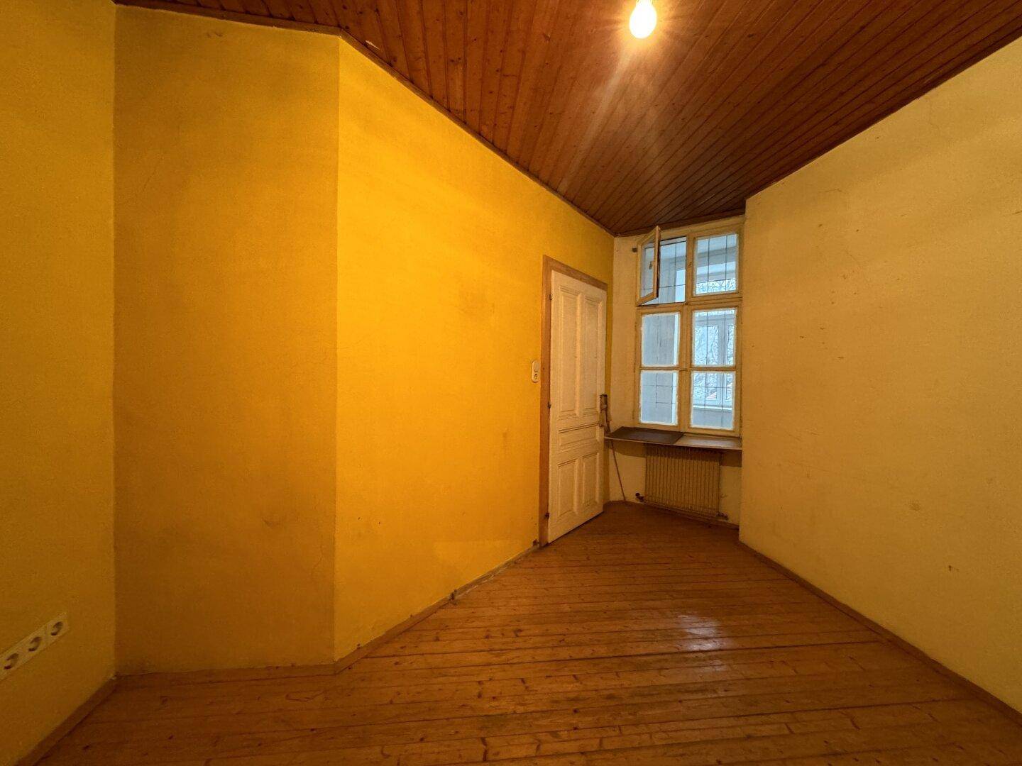 Heller Raum mit gelben Wänden, Holzdecke, Dielenboden und einem Fenster für natürliches Licht.