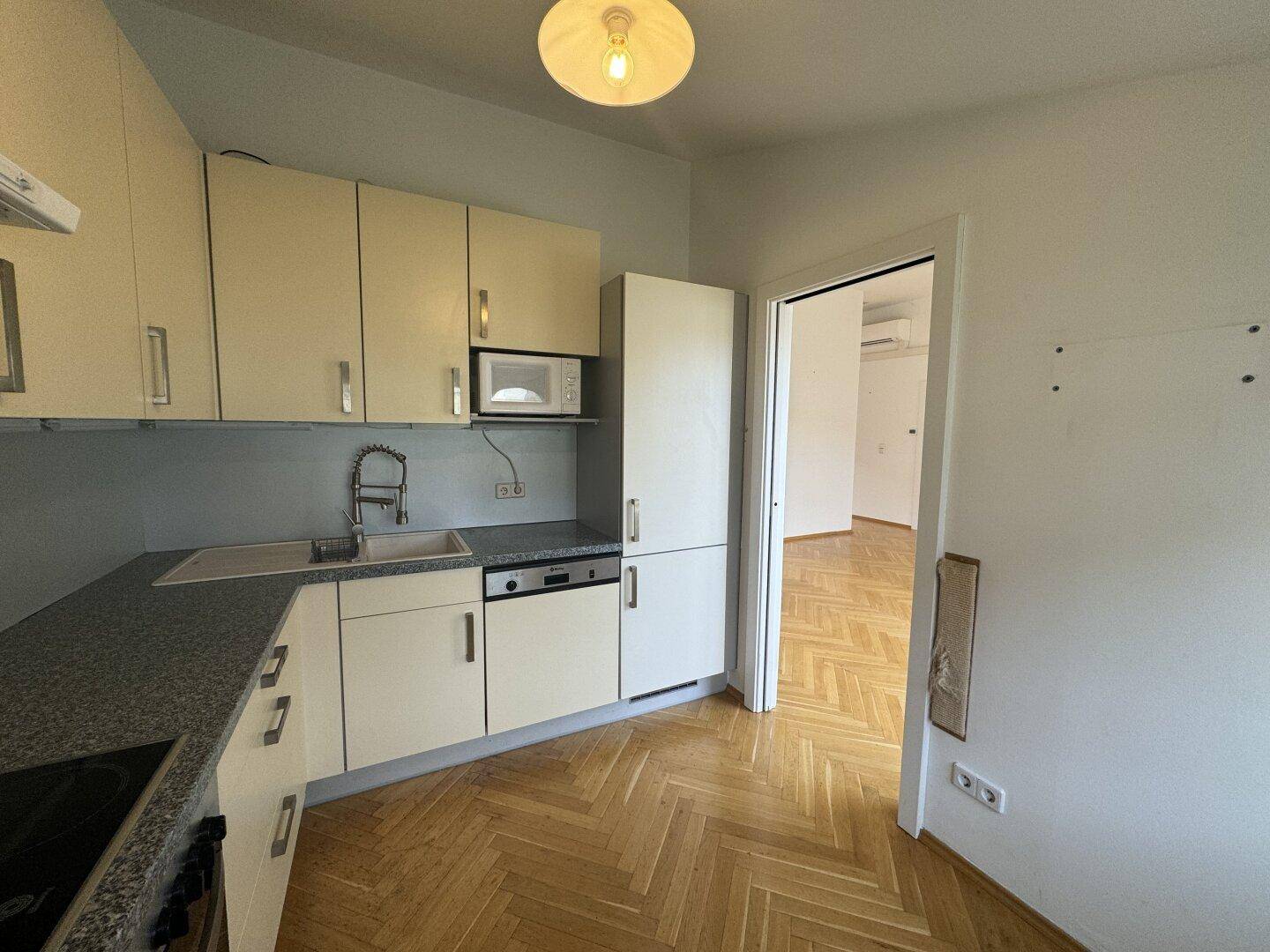 Funktionale Einbauküche mit hellen Fronten, dunkler Arbeitsplatte und integriertem Kühlschrank.