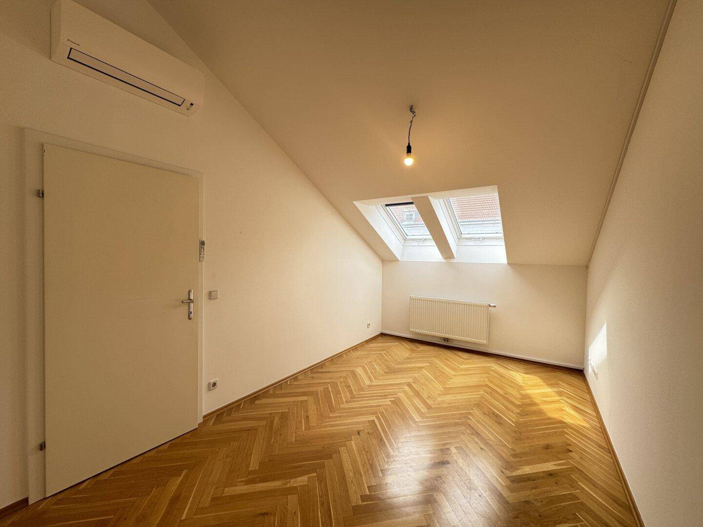 Helles Dachgeschosszimmer mit Parkettboden, schräger Decke und einem Dachfenster.