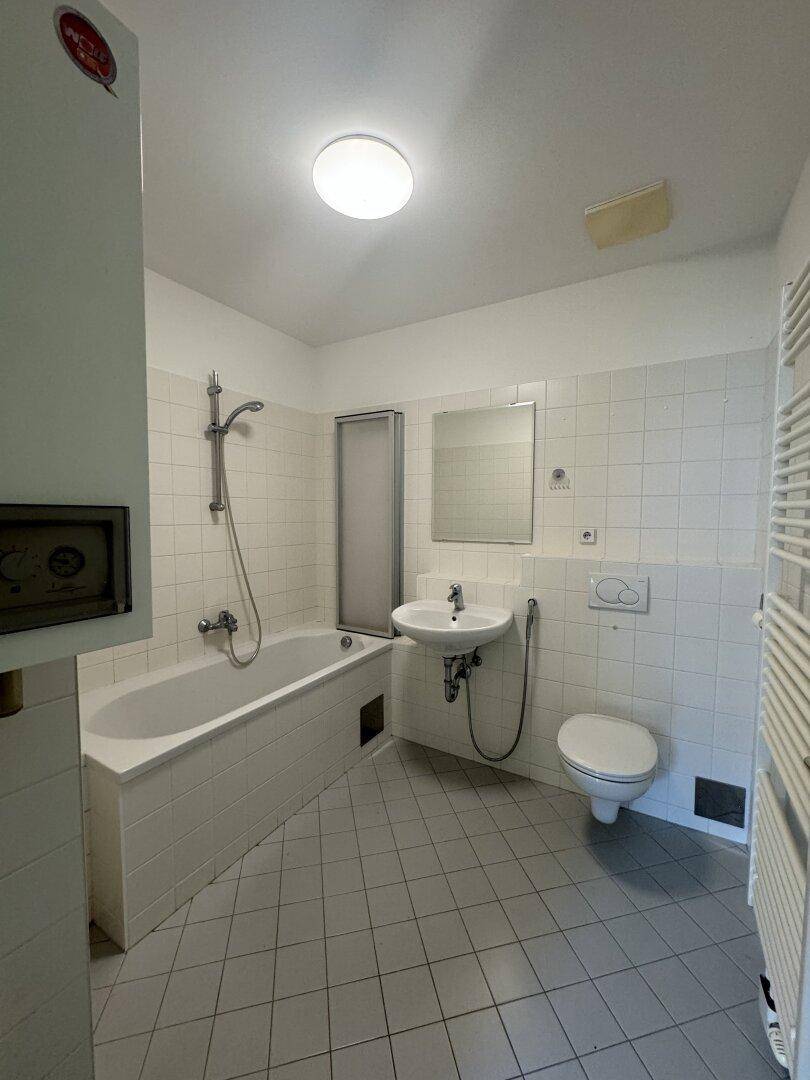 Badezimmer mit weißen Fliesen, Badewanne, Toilette, Waschbecken und Handtuchheizkörper.