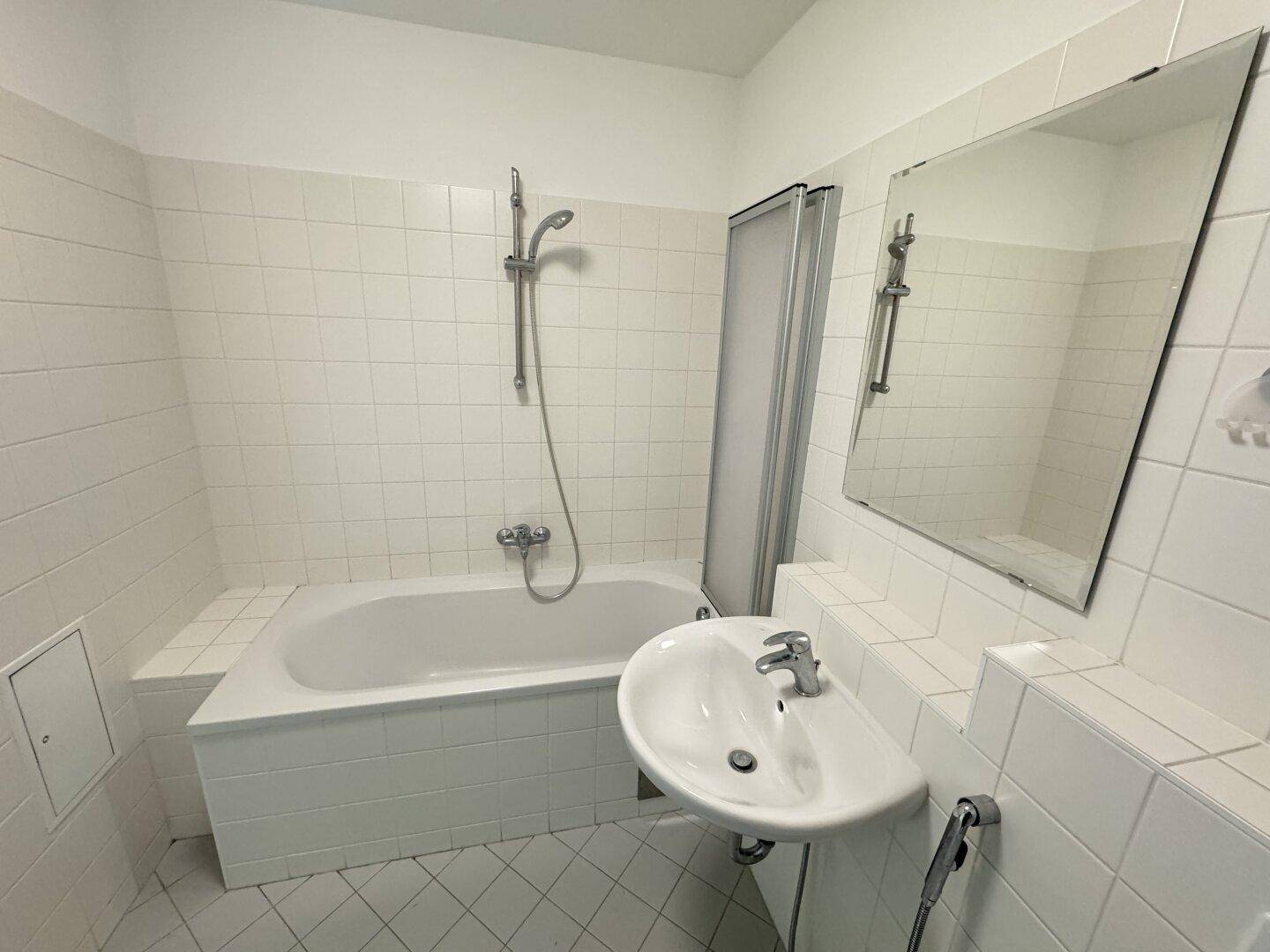 Helles Badezimmer mit weißen Fliesen, Badewanne und Waschbecken.