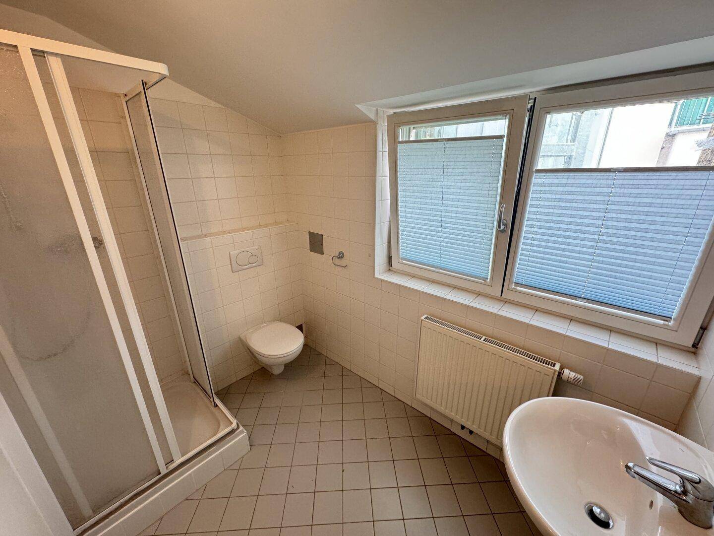 Badezimmer mit Duschkabine, Toilette, Waschbecken und Fenster für natürliche Belüftung.