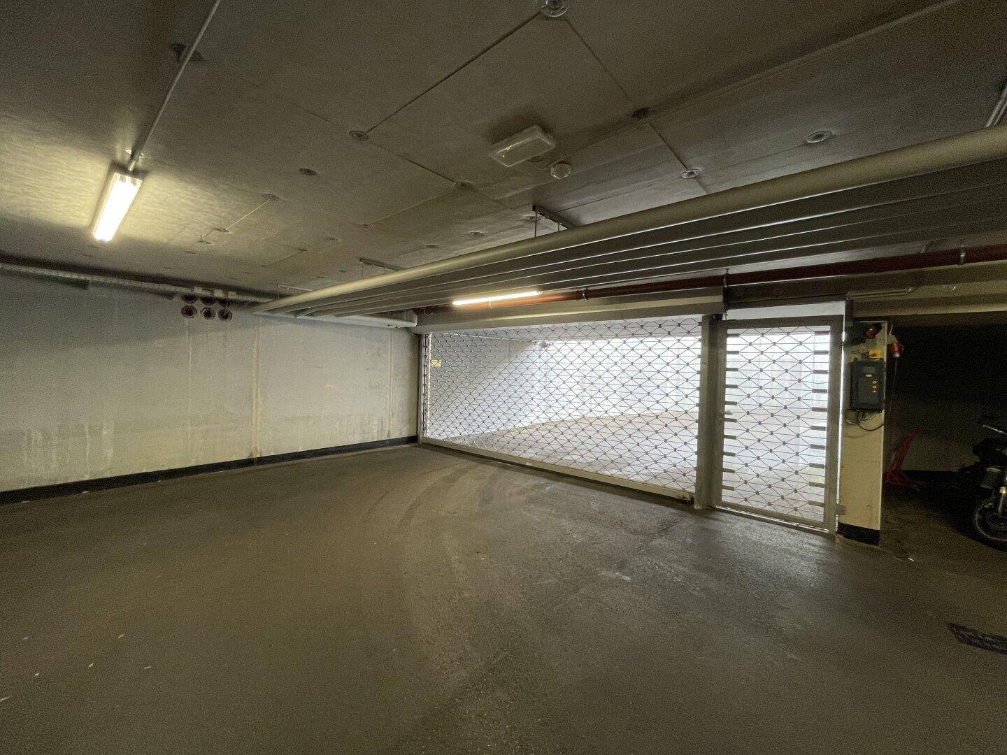 Eingangsbereich einer Tiefgarage mit Rolltor und technischer Installation an der Wand.