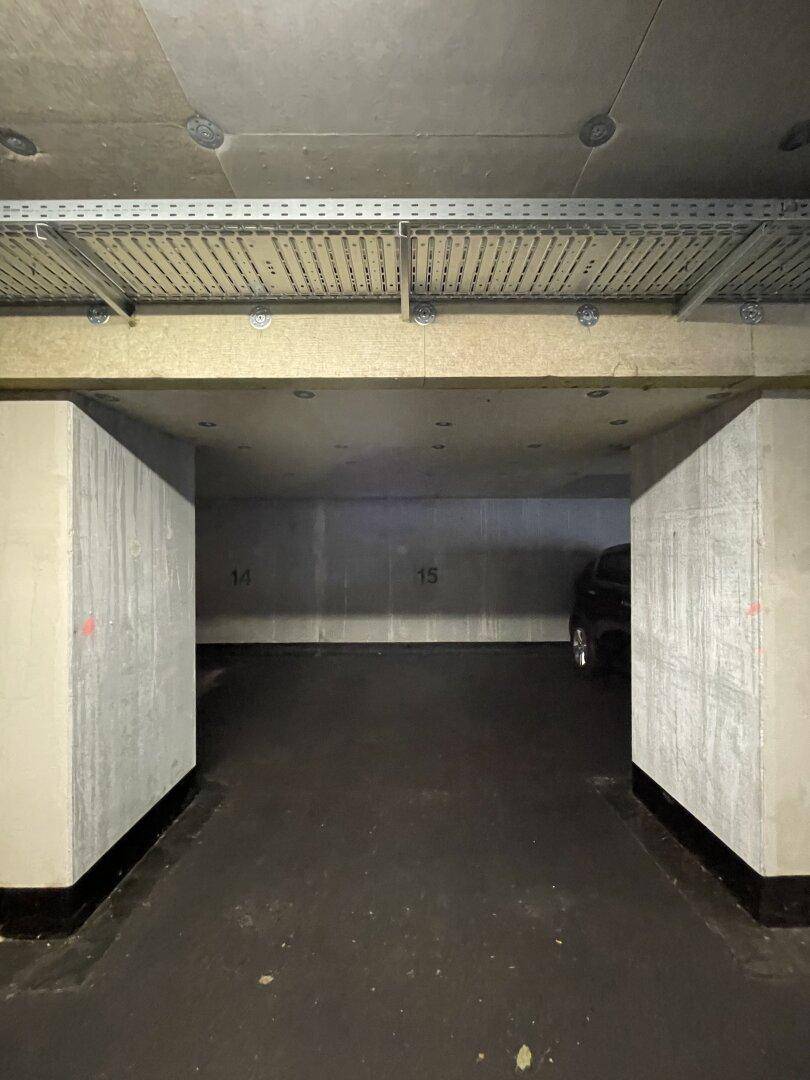 Leerer Stellplatz in einer Tiefgarage mit Betonpfeilern und Deckeninstallationen.