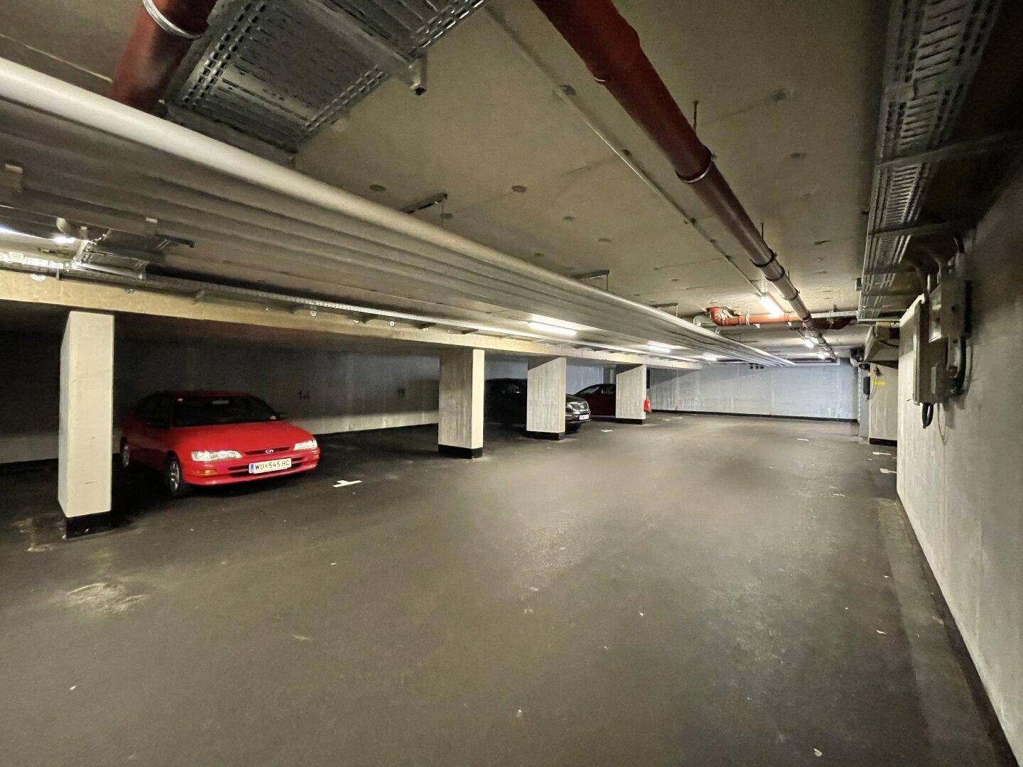 Weitläufige Tiefgarage mit mehreren geparkten Fahrzeugen und sichtbaren Leitungen an der Decke.