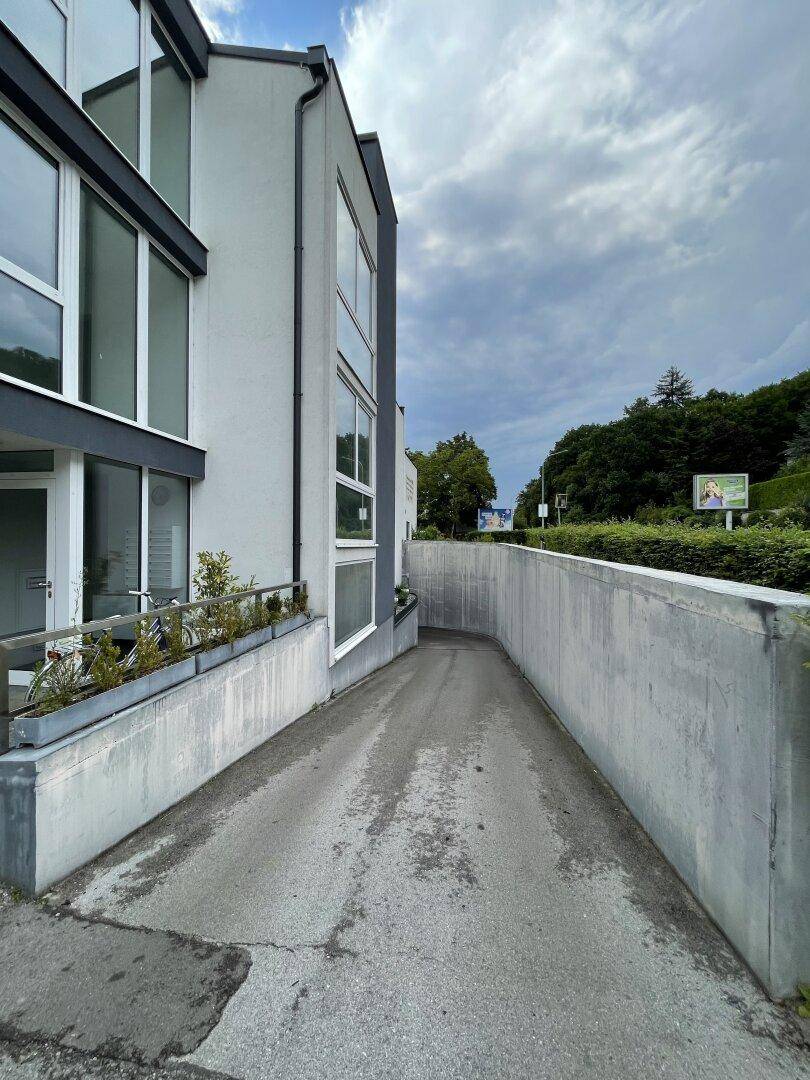 Modernes Gebäude mit Zufahrt zu einer Tiefgarage unter bewölktem Himmel.