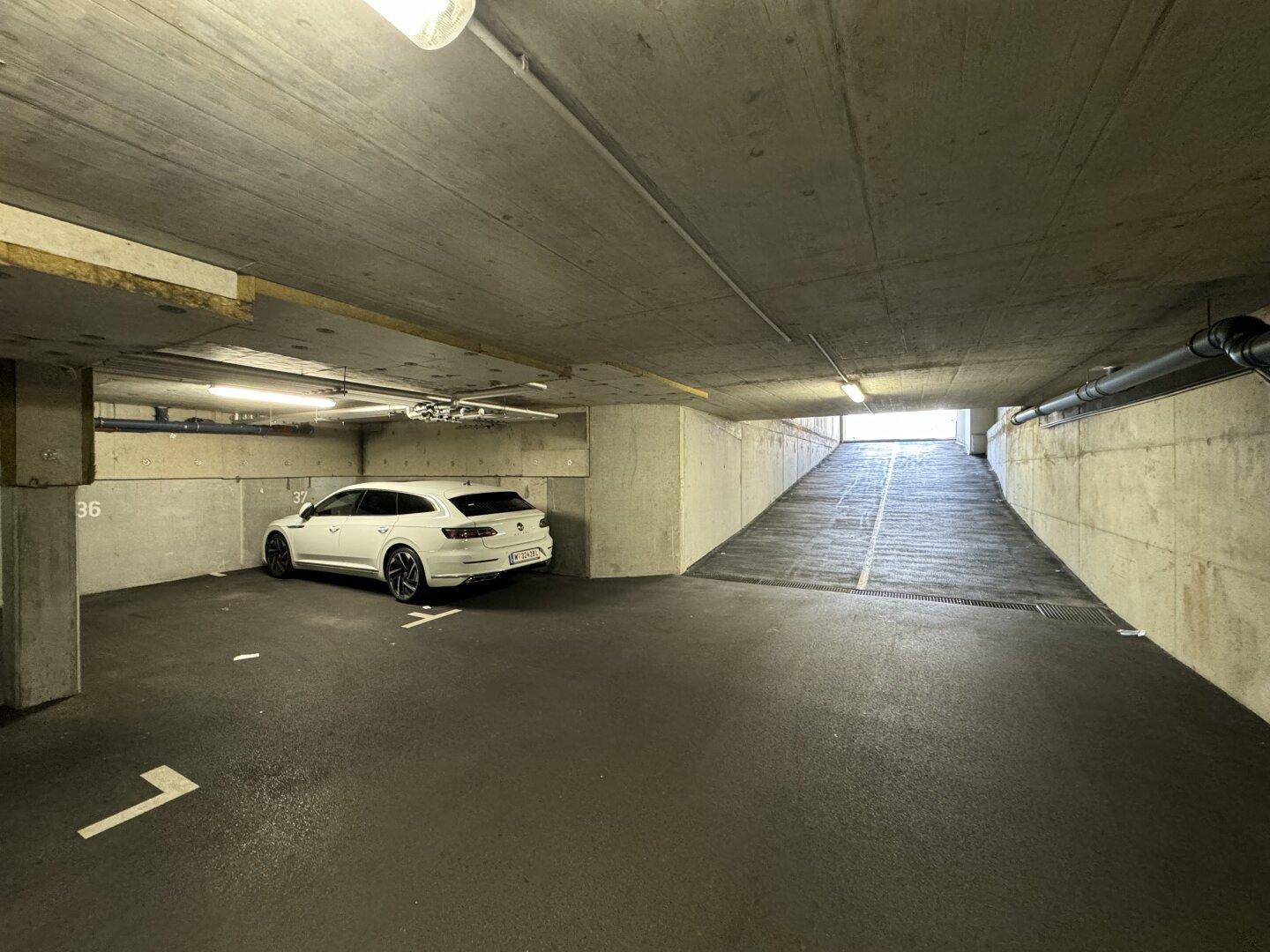 Geräumige Tiefgarage mit einem geparkten weißen Auto und der Ausfahrt im Hintergrund.