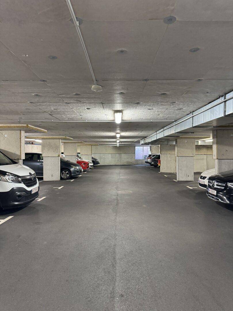 Weitläufige Tiefgarage mit mehreren geparkten Autos und Betonstützen.